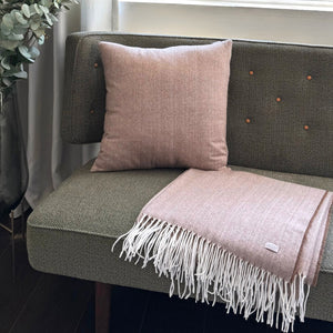 Pink throw blanket and pillow on a green sofa with a plant in the background