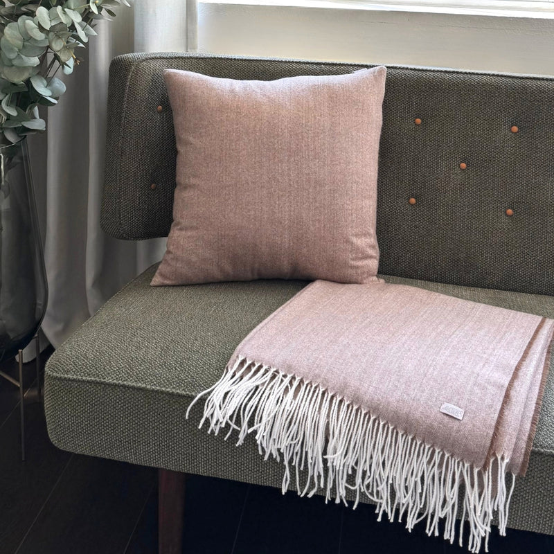 Pink throw blanket and pillow on a green sofa with a plant in the background